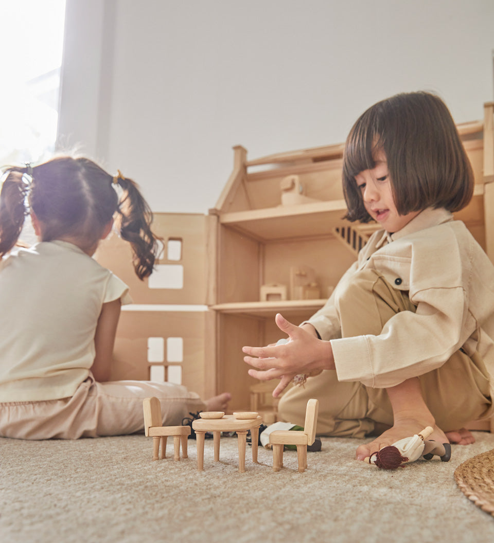 Two children sat on the floor playing with the PlanToys wooden Victorian furniture dollhouse set