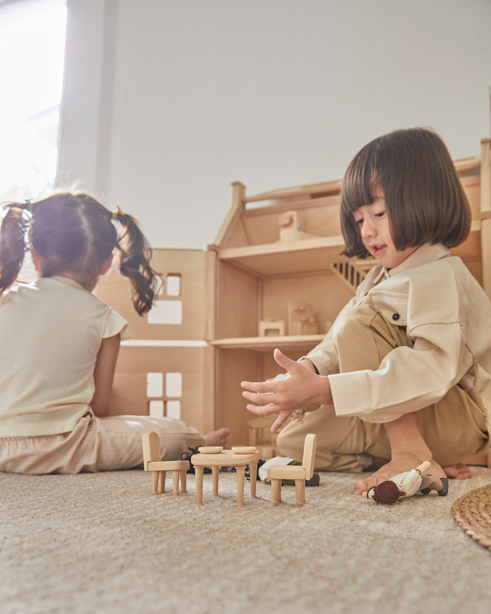 Two children sat on the floor playing with the PlanToys wooden Victorian furniture dollhouse set