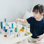 Young girl playing with the PlanToys plastic-free wooden city blocks on a white bed