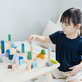 Young girl playing with the PlanToys plastic-free wooden city blocks on a white bed