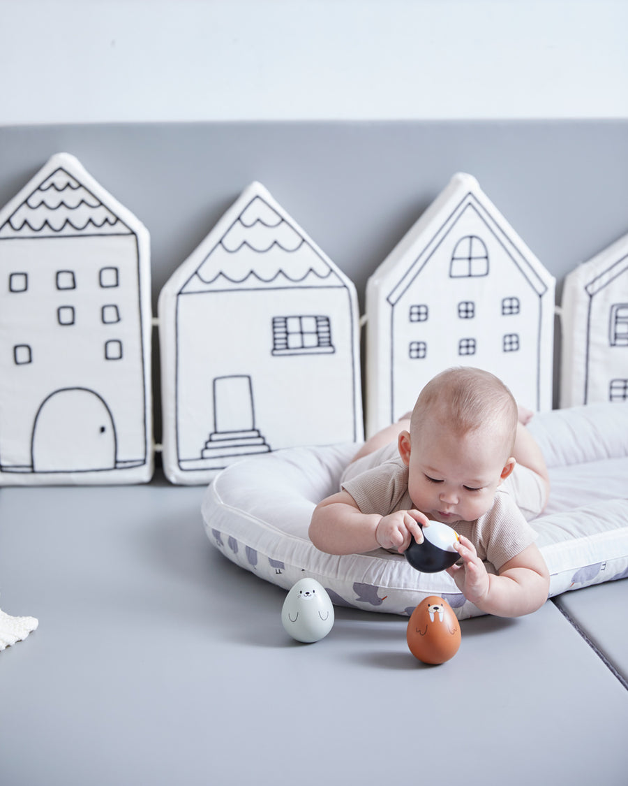 Baby laying on a white cushion looking at the PlanToys wobbly walrus