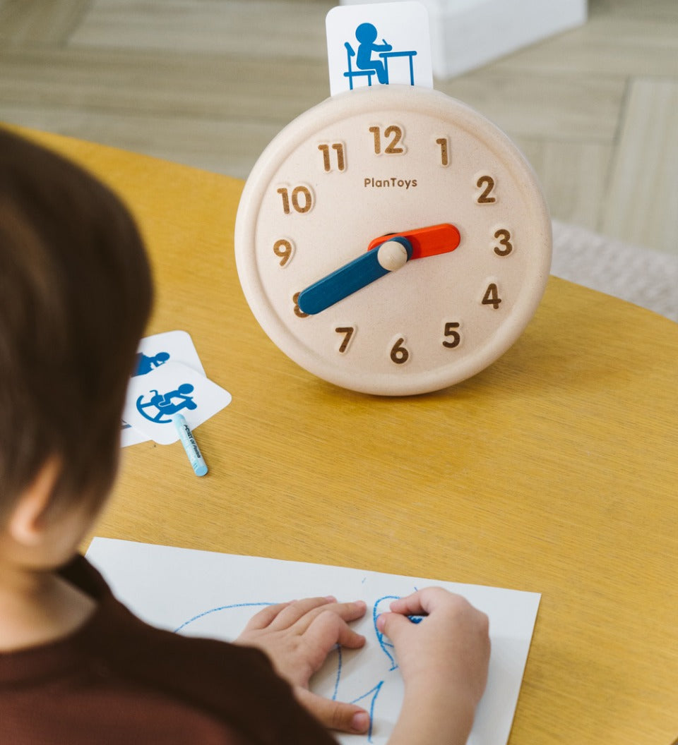 Close up of child drawing on some paper next to the PlanToys wooden activities clock