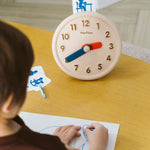 Close up of child drawing on some paper next to the PlanToys wooden activities clock