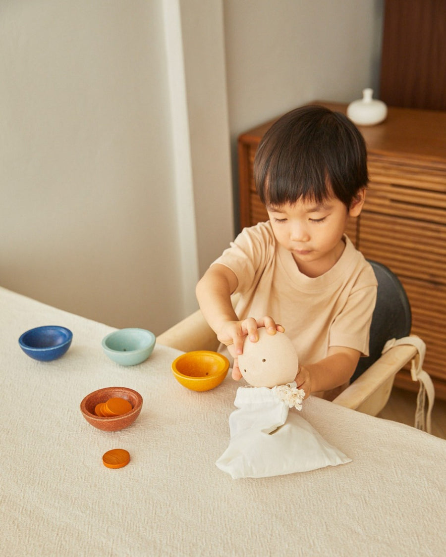 Young boy putting a PlanToys wooden Waldorf cup into its drawstring bag