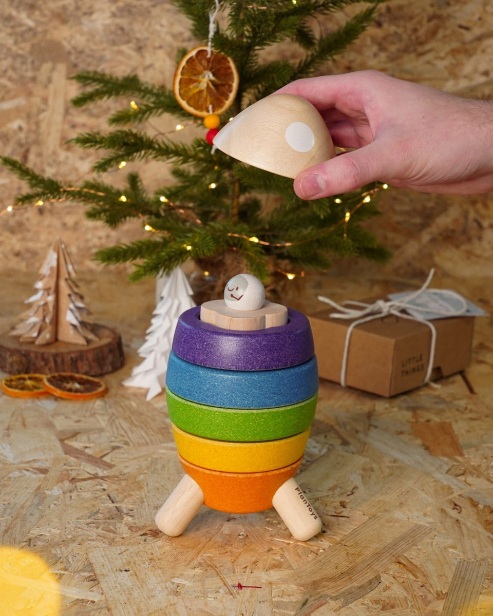 Close up of hand holding a piece of the PlanToys wooden stacking rocket toy above the astronaut