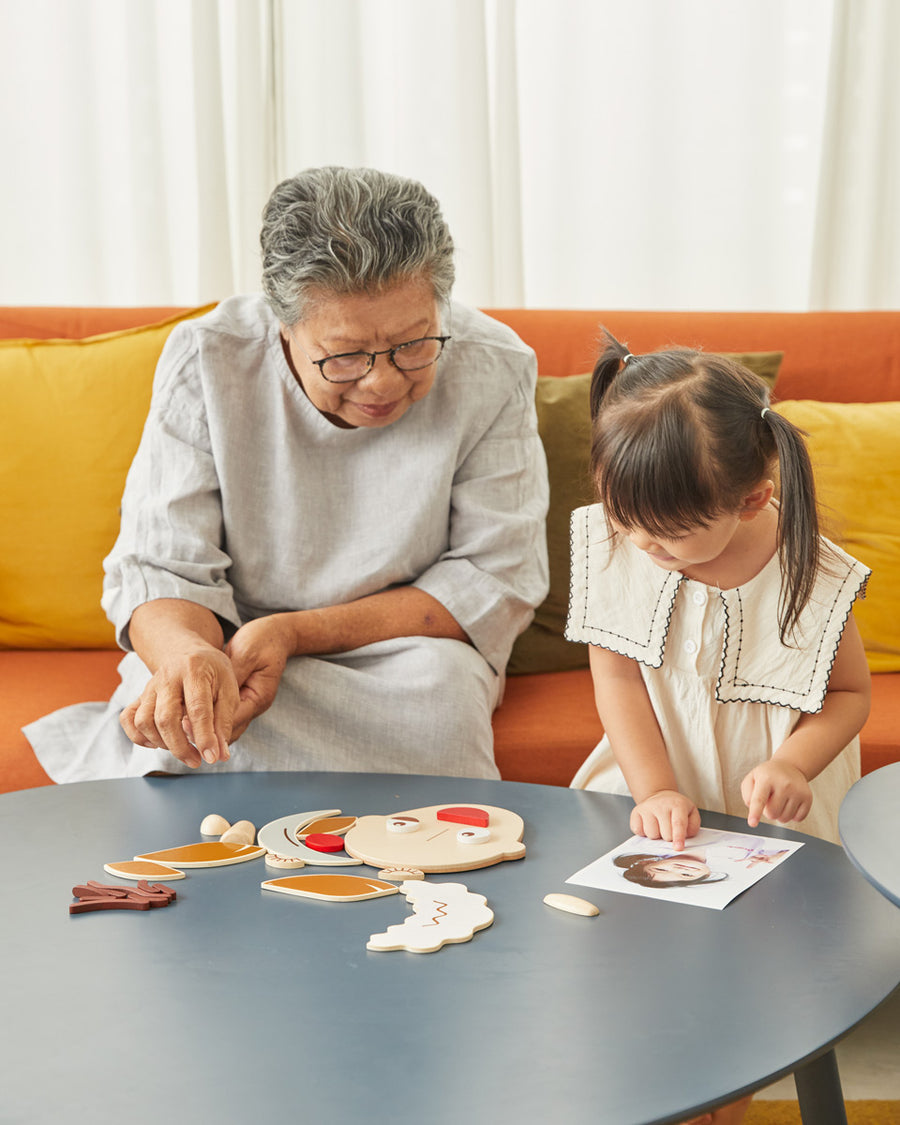 Woman and young girl playing with the PlanToys wooden build a face toy set on a wooden table