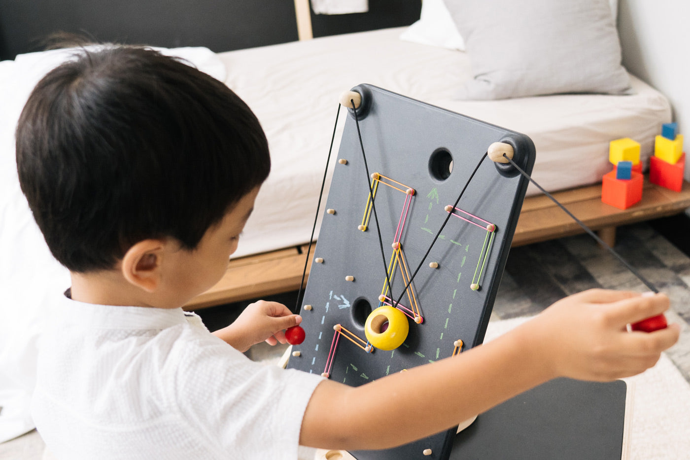 Close up of a child pulling the strings on the PlanToys wall ball game to make the ball move up the board.