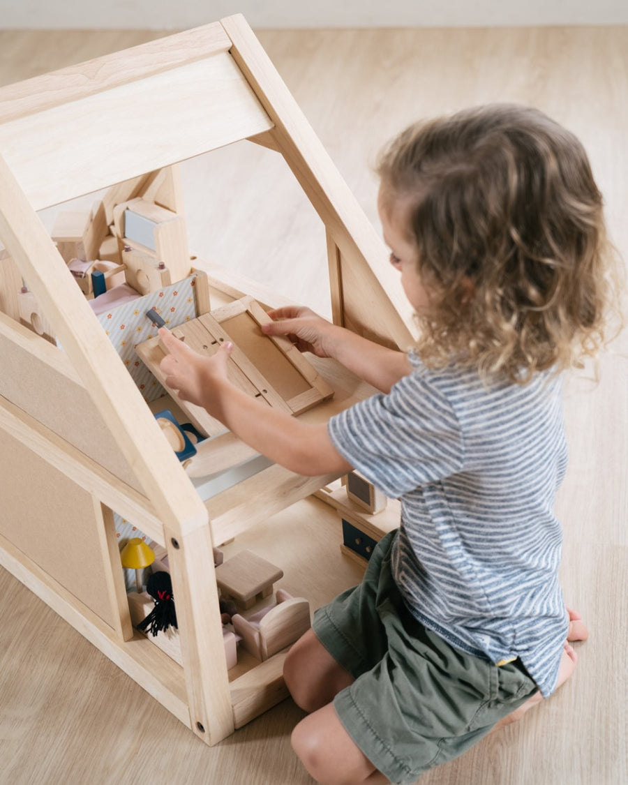 Young boy kneeling down playing inside the PlanToys eco-friendly wooden dollhouse set on a wooden floor