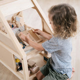 Young boy kneeling down playing inside the PlanToys eco-friendly wooden dollhouse set on a wooden floor