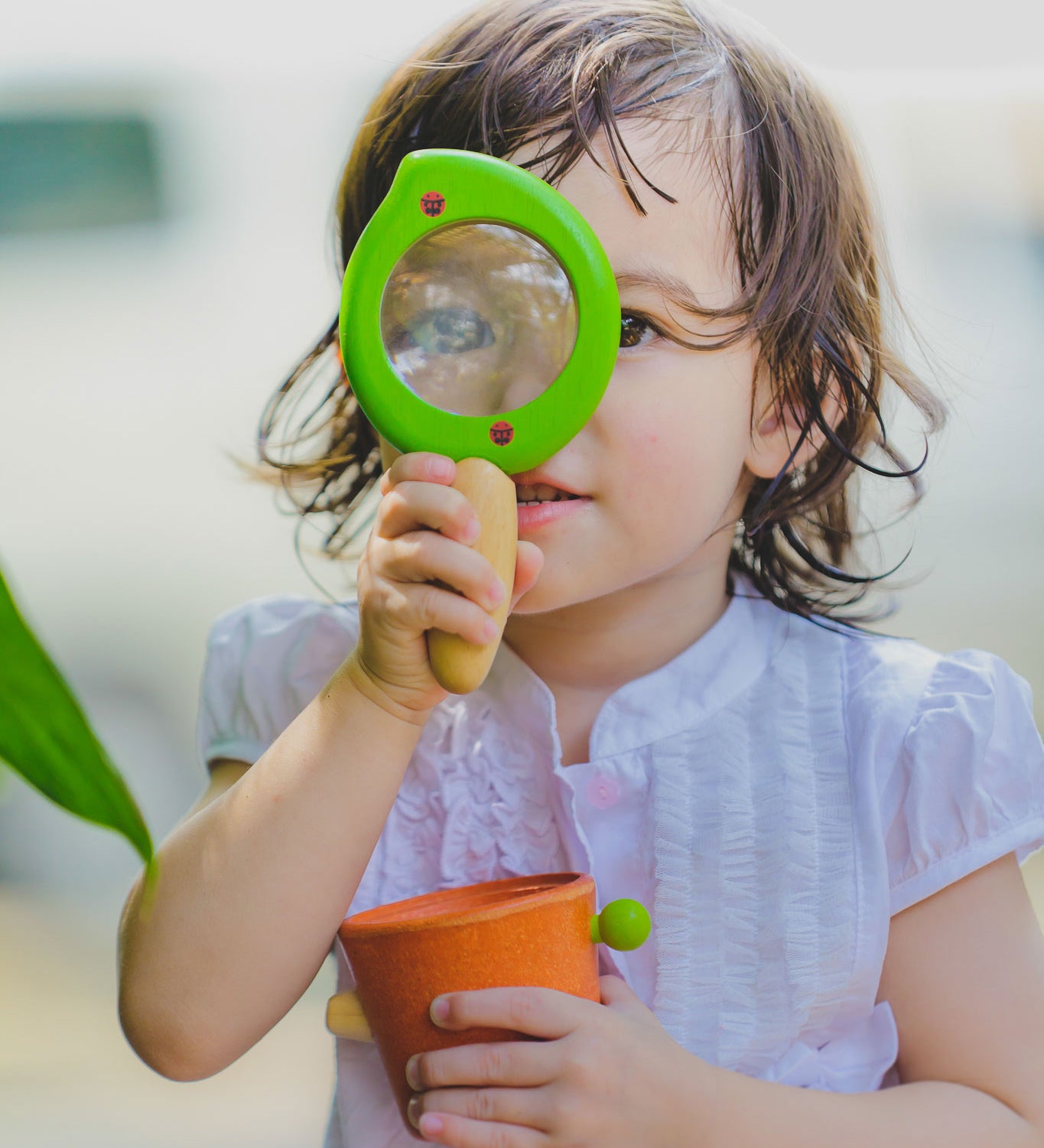 A child holding the Plan Toys Leaf Magnifier up to their eye. 