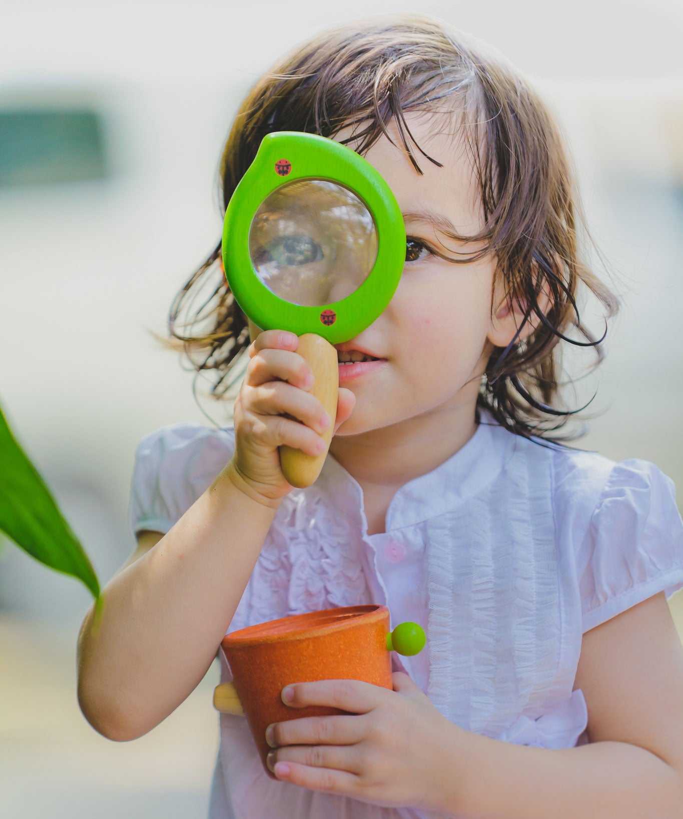 A child holding the Plan Toys Leaf Magnifier up to their eye. 