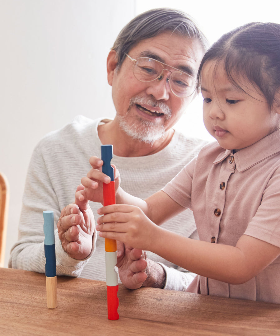 A child and adult sitting at a wooden table stacking blocks from the PlanToys plastic-free logs puzzle.