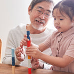 A child and adult sitting at a wooden table stacking blocks from the PlanToys plastic-free logs puzzle.