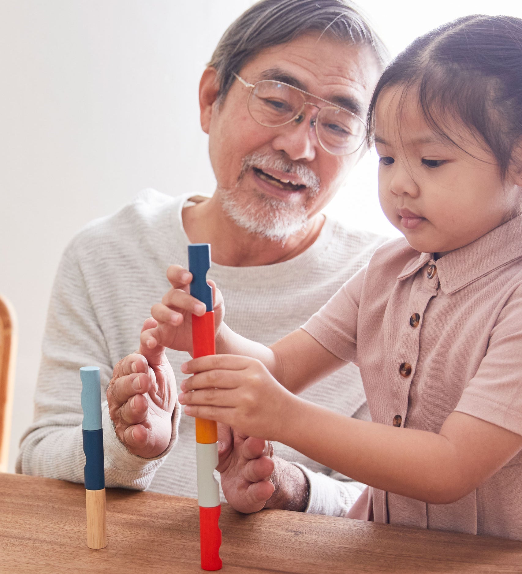 A child and adult sitting at a wooden table stacking blocks from the PlanToys plastic-free logs puzzle.