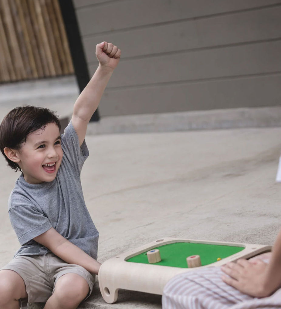 A child playing with the PlanToys Magnetic Board Game, he has his fist in the air with a smile on his face. 
