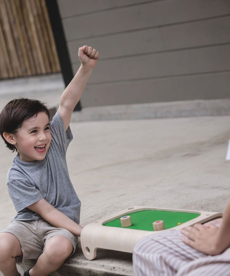 A child playing with the PlanToys Magnetic Board Game, he has his fist in the air with a smile on his face. 
