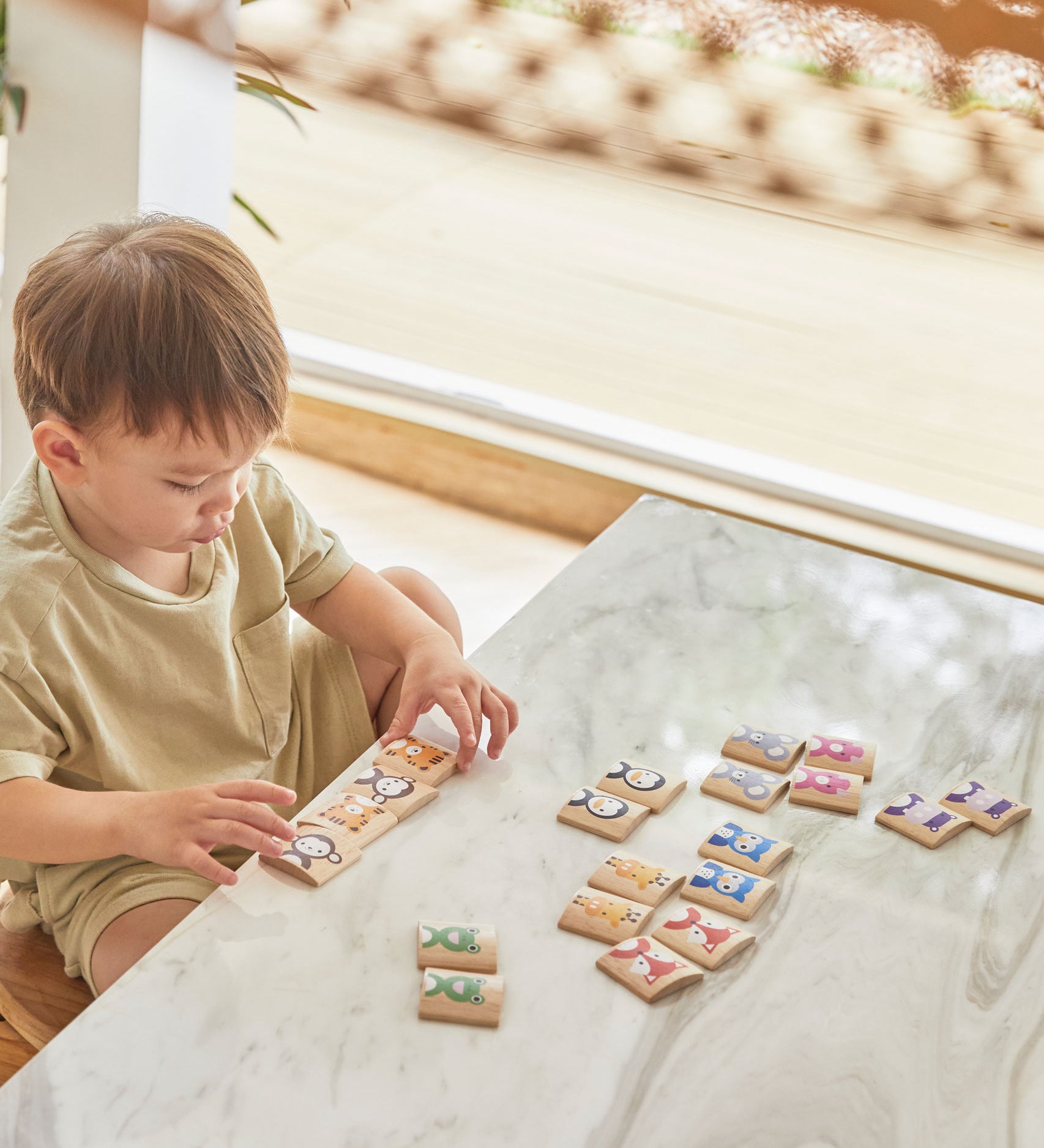 A child sitting at a white marble table playing with the PlanToys Matching Animals Memory Game. 