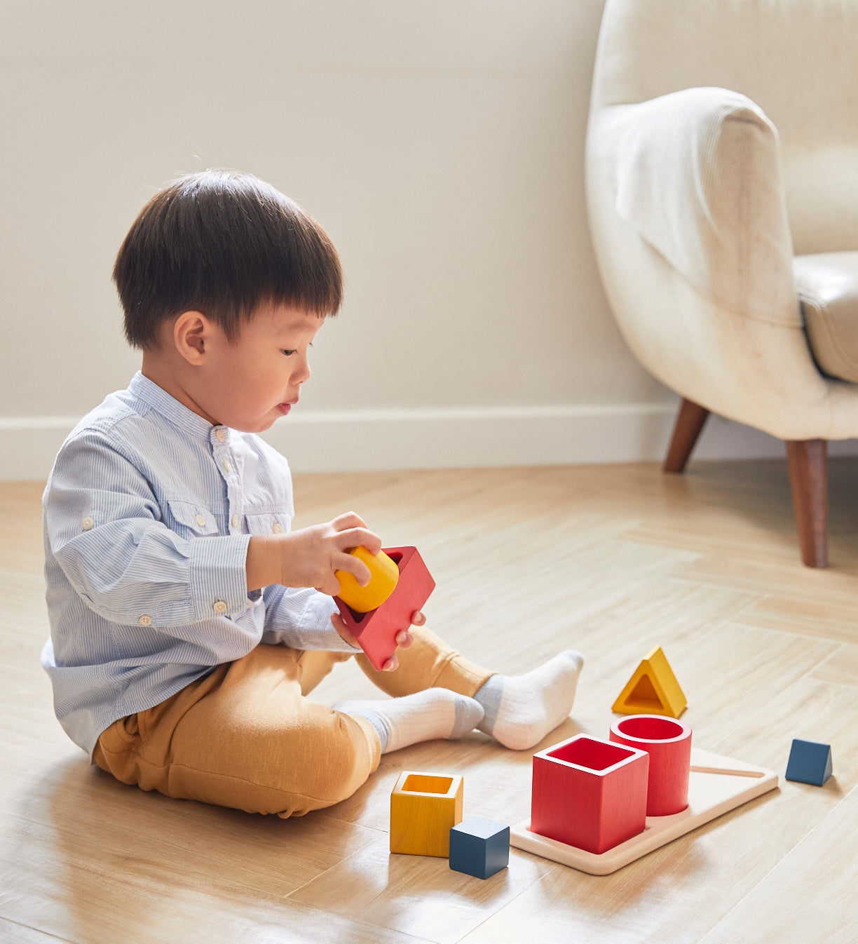 A child sitting on a wooden floor playing with the PlanToys Matching & Nesting Shapes Puzzle.