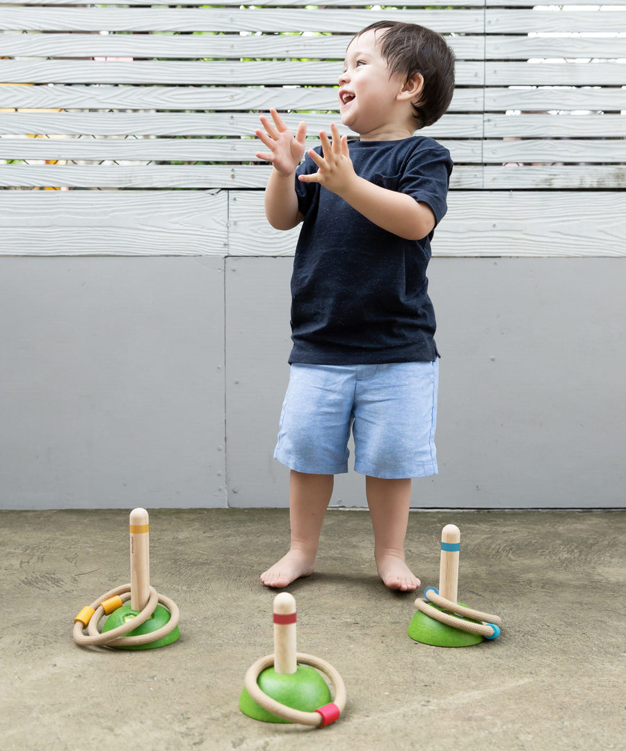 A child clapping their hand with delight whilst playing with the PlanToys Meadow Ring Toss game. 
