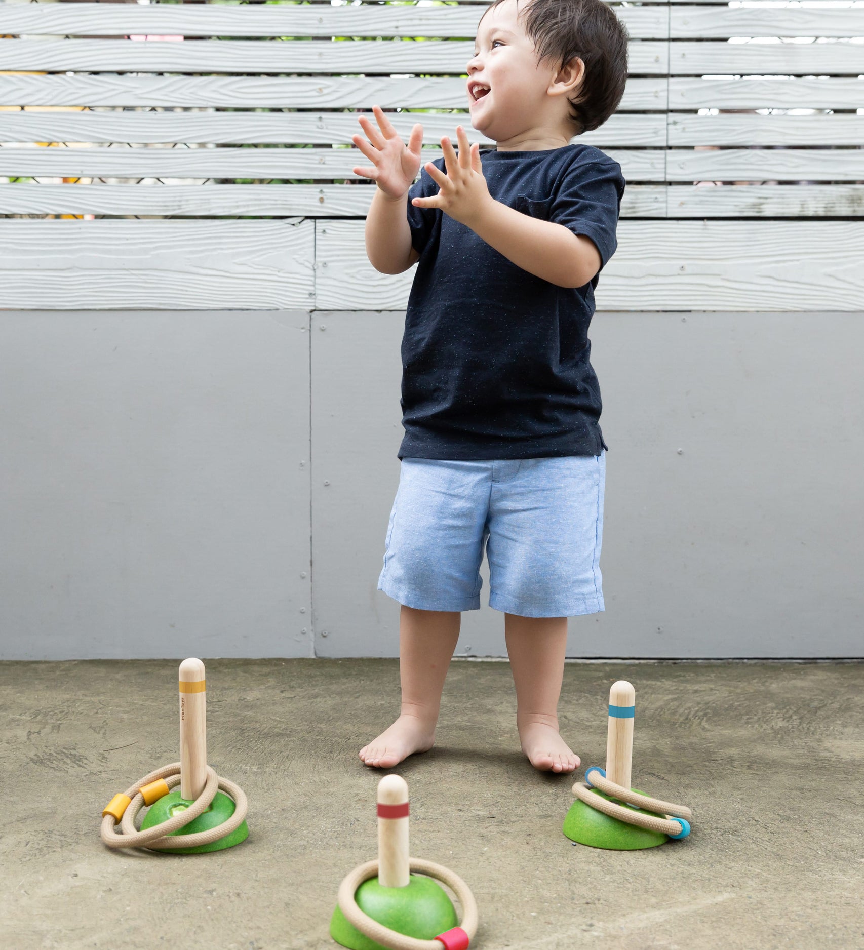 A child clapping their hand with delight whilst playing with the PlanToys Meadow Ring Toss game. 
