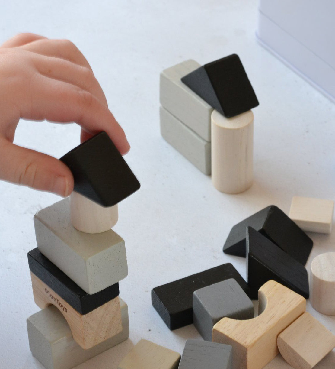 A close up of a child's hand laying with the blocks from the Plan Toys Mini Construction Set.