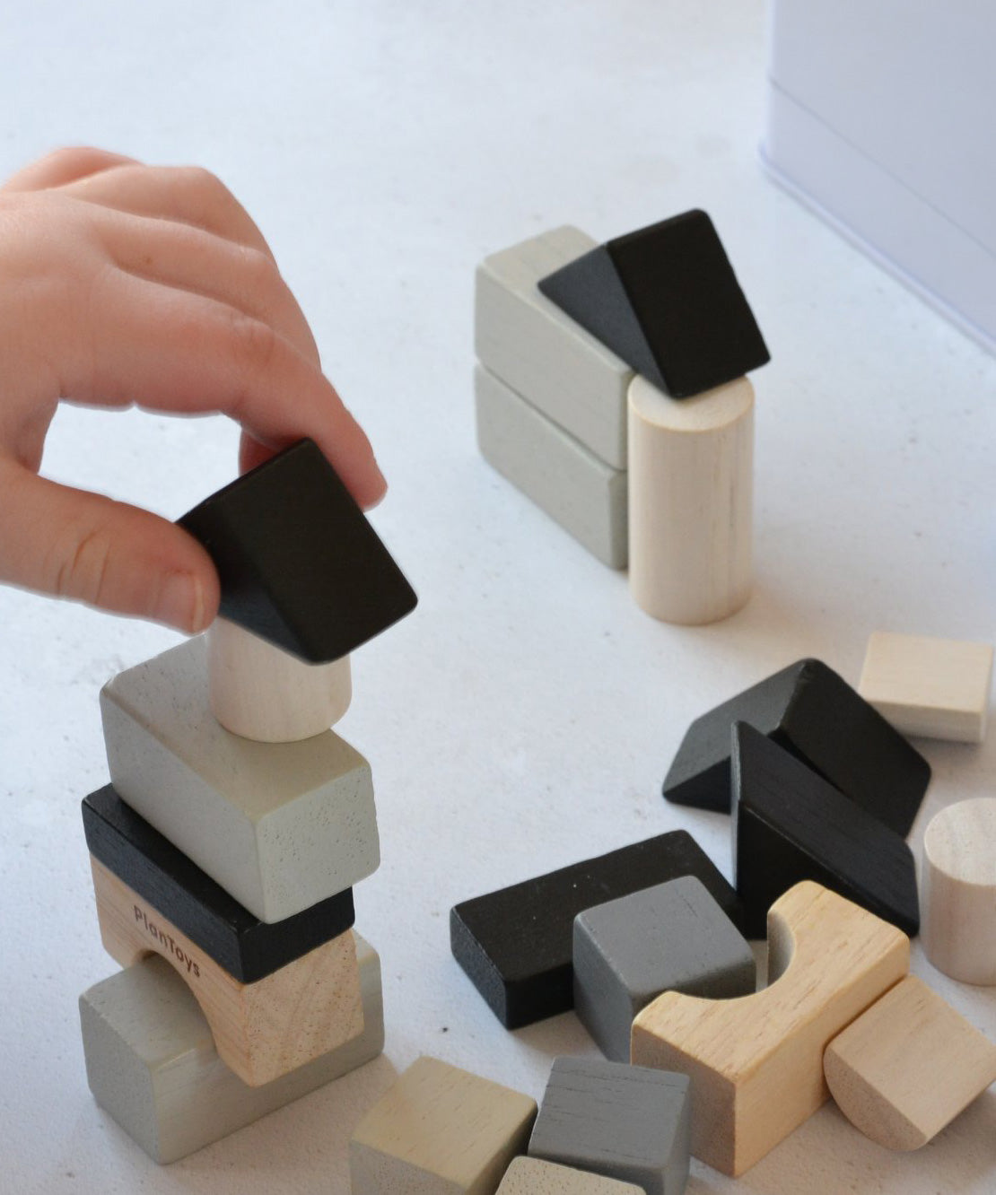 A close up of a child's hand laying with the blocks from the Plan Toys Mini Construction Set.