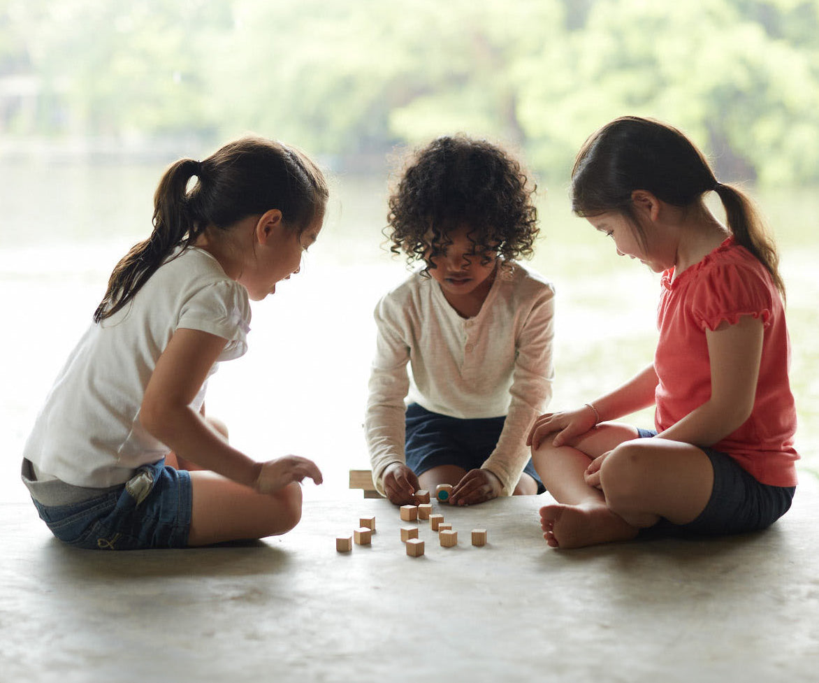 Three children sitting on the floor playing with the PlanToys Mini Memo Game set. 