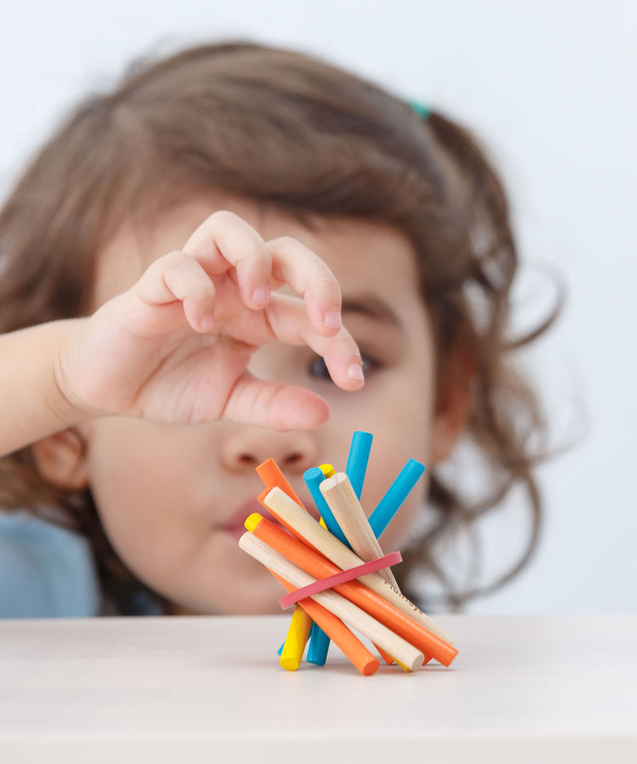 A close up of child's hands in the pincer grip position reaching for a blue stick from the PlanToys Mini Pick-Up Sticks.
