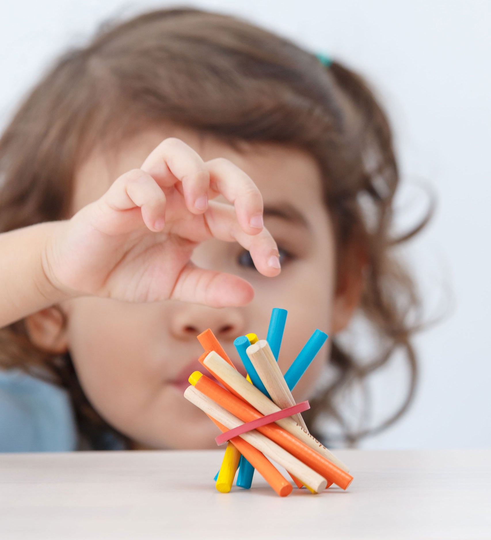 A close up of child's hands in the pincer grip position reaching for a blue stick from the PlanToys Mini Pick-Up Sticks.
