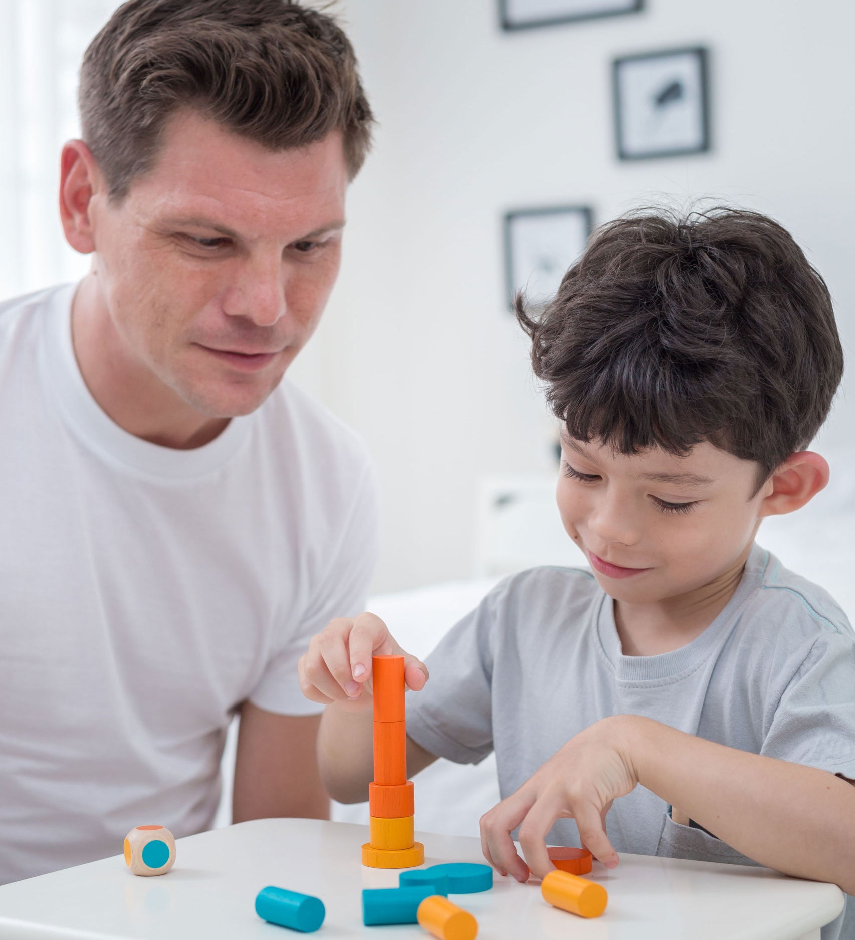 An adult and a child sitting at a table playing with the PlanToys Mini Stacking Game.