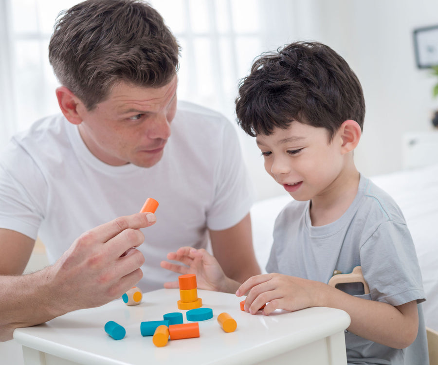 An adult and a child sitting at a table playing with the PlanToys Mini Stacking Game.