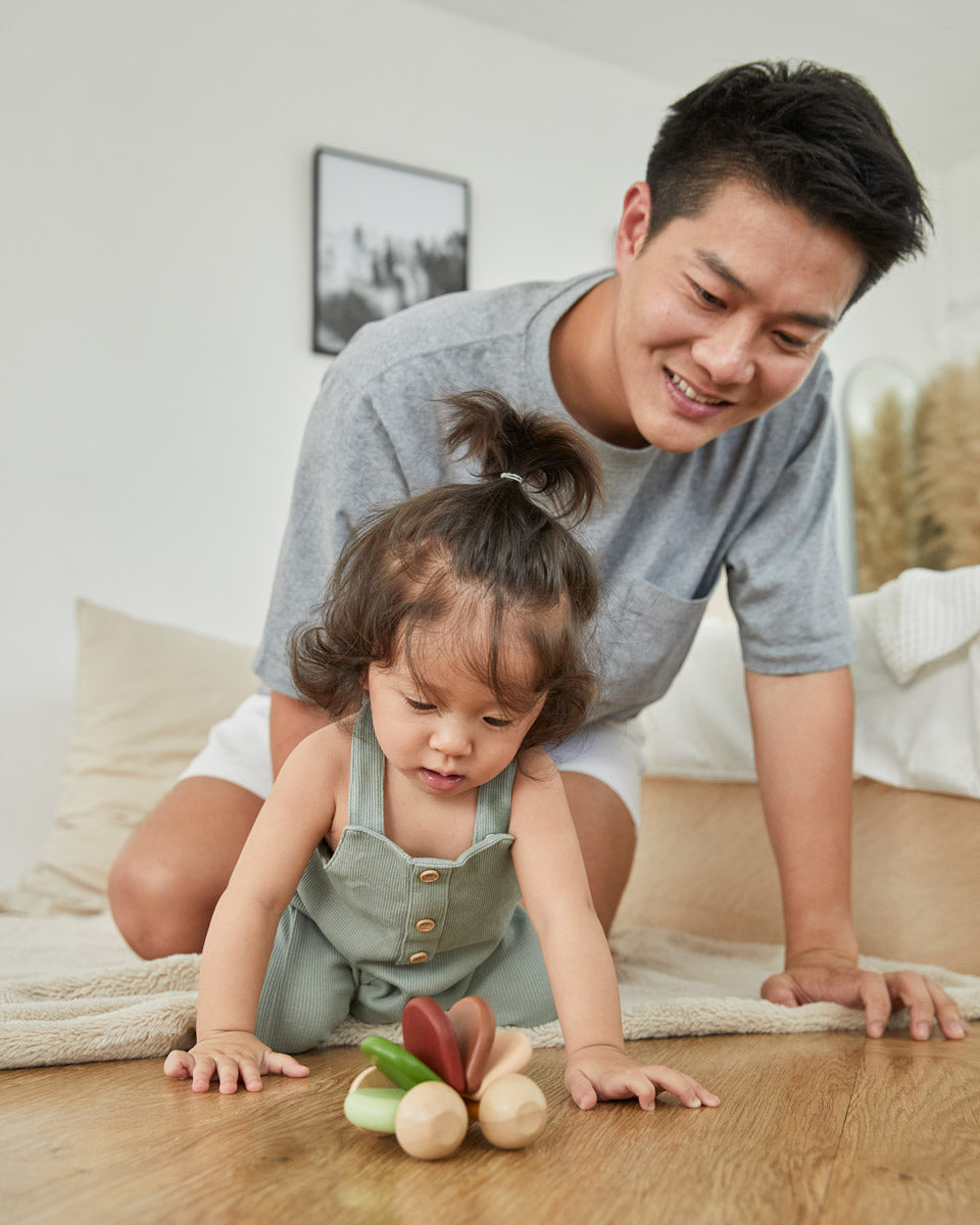 Young girl and man kneeling down looking at the PlanToys wooden baby car toy