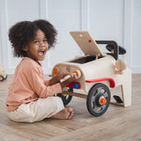 A child playing with the PlanToys Motor Mechanic. The child is tinkering with the headlights using one of the tools and has a big smile on their face.  
