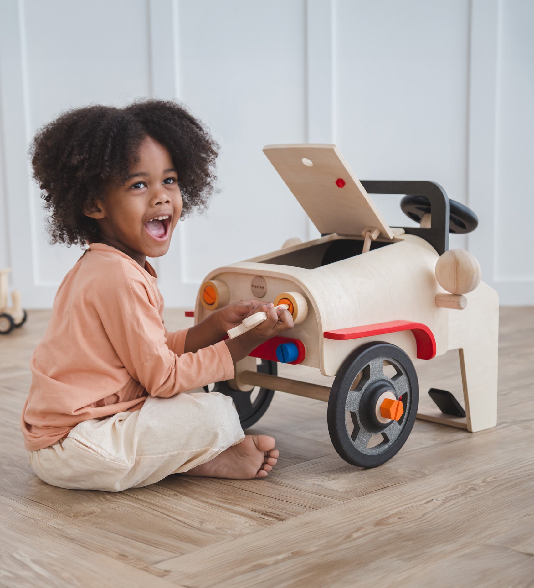 A child playing with the PlanToys Motor Mechanic. The child is tinkering with the headlights using one of the tools and has a big smile on their face.  
