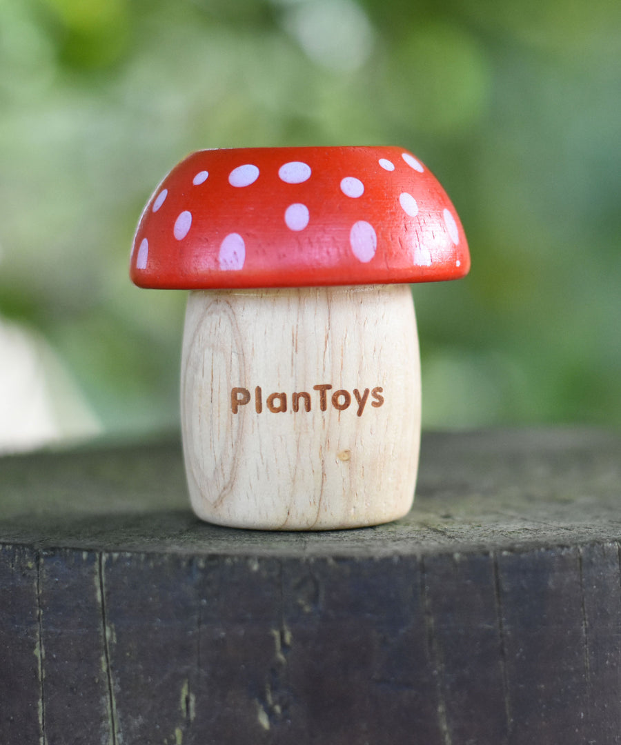 A red PlanToys Mushroom Kaleidoscope on a round fence post outdoors. 