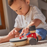 Young boy sat on a carpet playing with the PlanToys wooden pull along drummer