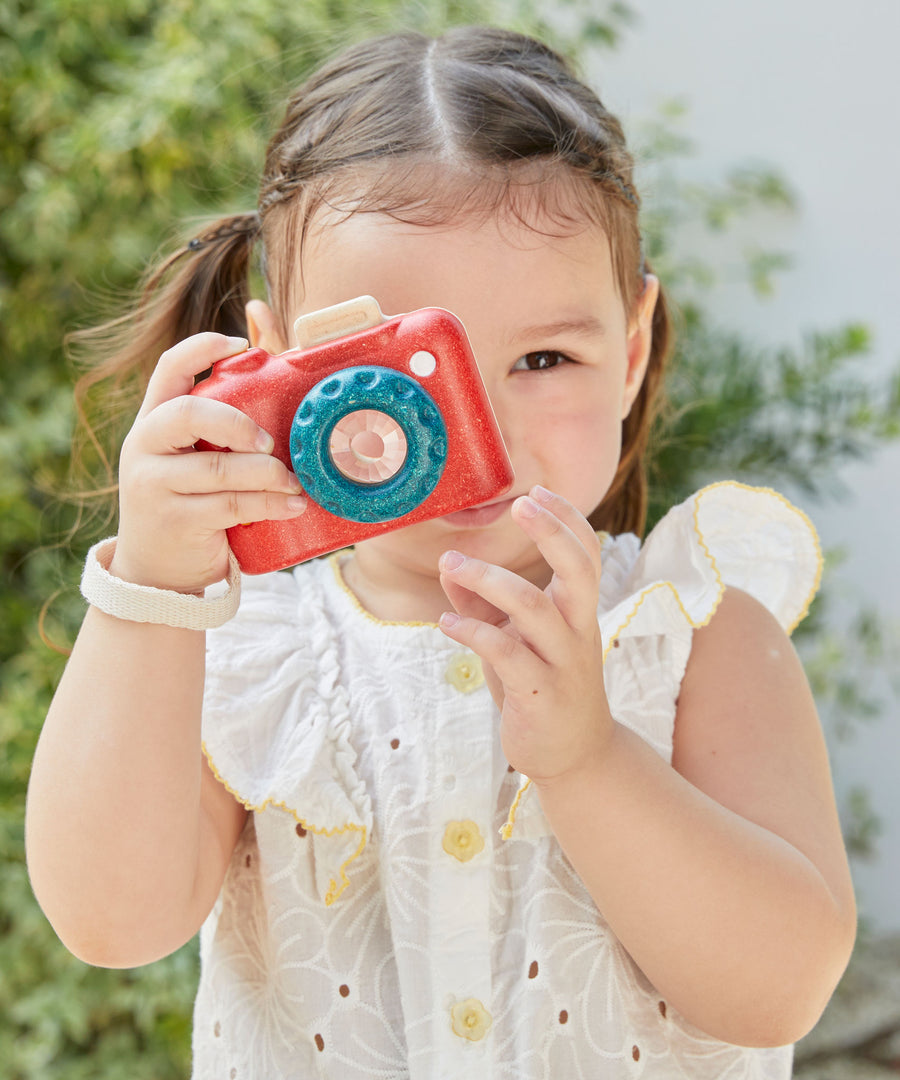 A child playing with a Plan Toys My First Camera, they are holding it up to their eye ready to snap away. 