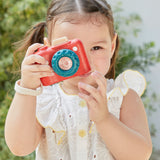 A child playing with a Plan Toys My First Camera, they are holding it up to their eye ready to snap away. 