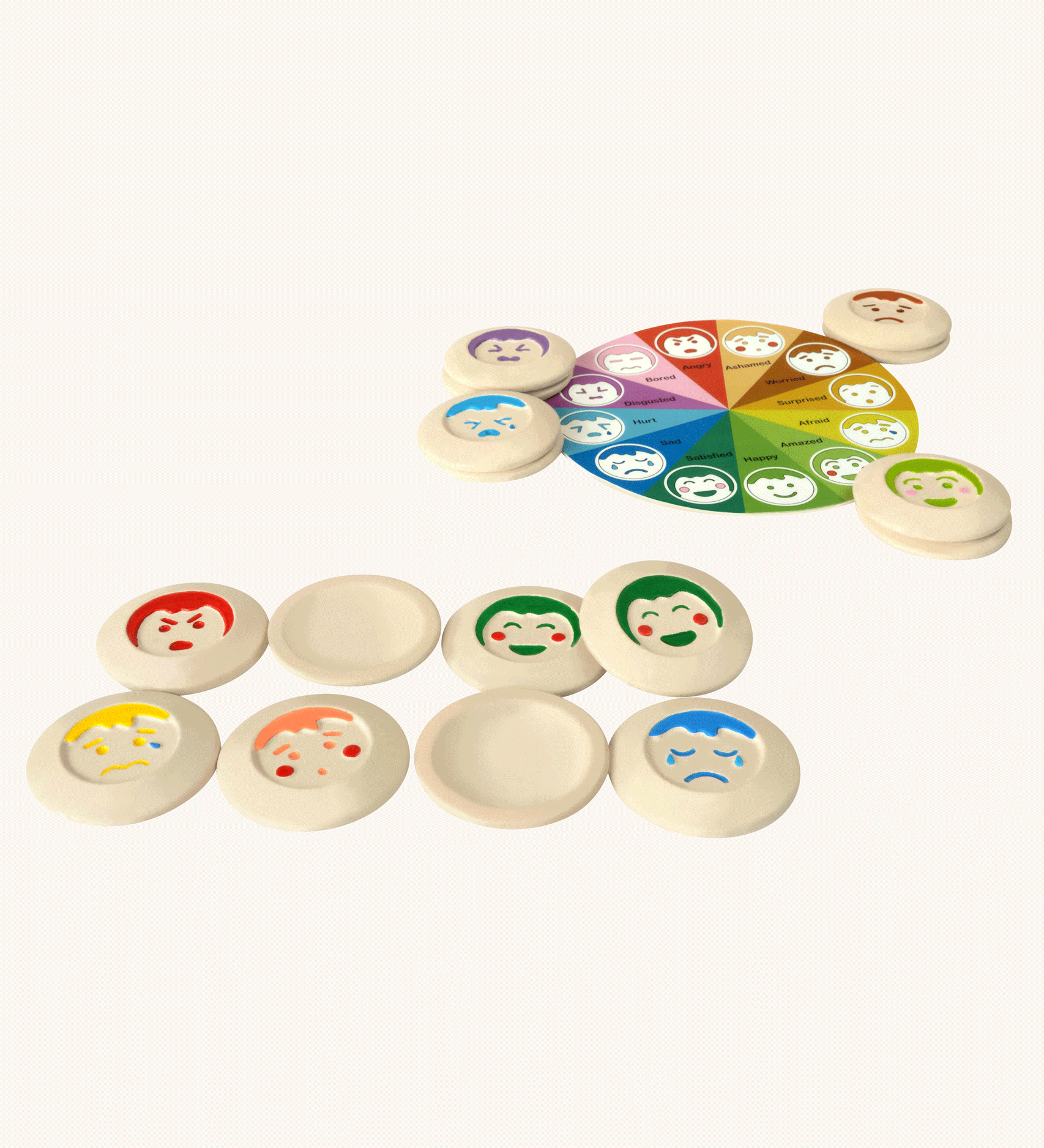 The PlanToys My Mood Memo game on a plain background. Some of the emotions discs are placed at the front some are upside down, showing the plain curved sides. The wheel of emotions can be seen in the background. 
