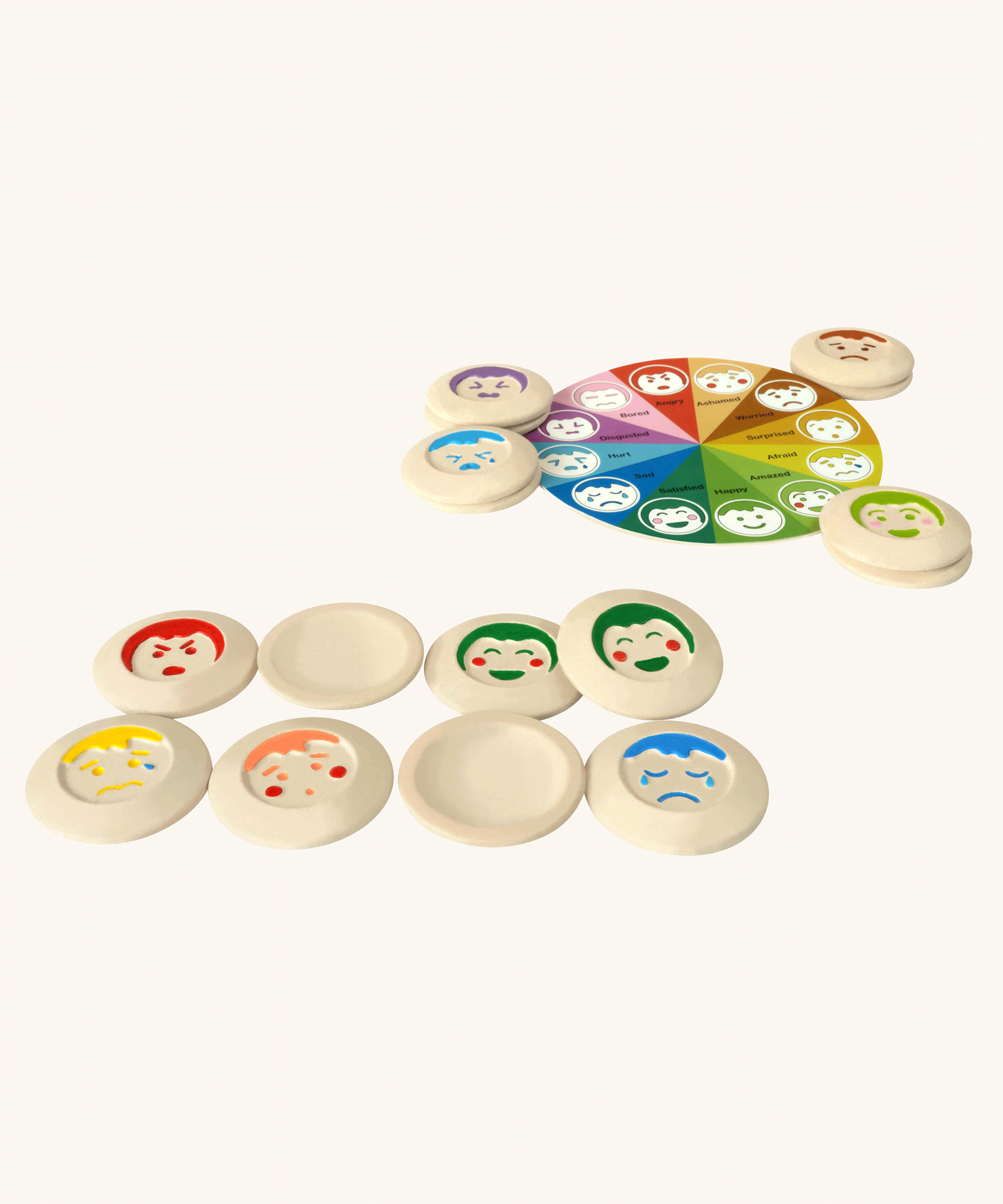 The PlanToys My Mood Memo game on a plain background. Some of the emotions discs are placed at the front some are upside down, showing the plain curved sides. The wheel of emotions can be seen in the background. 
