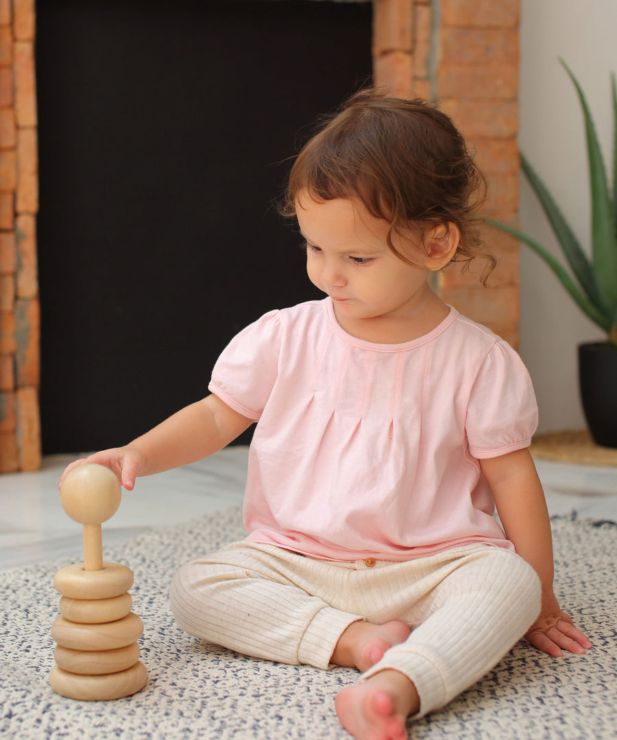 A child sitting on a blue and white rug playing with the Plan Toys Natural Stacking Ring.