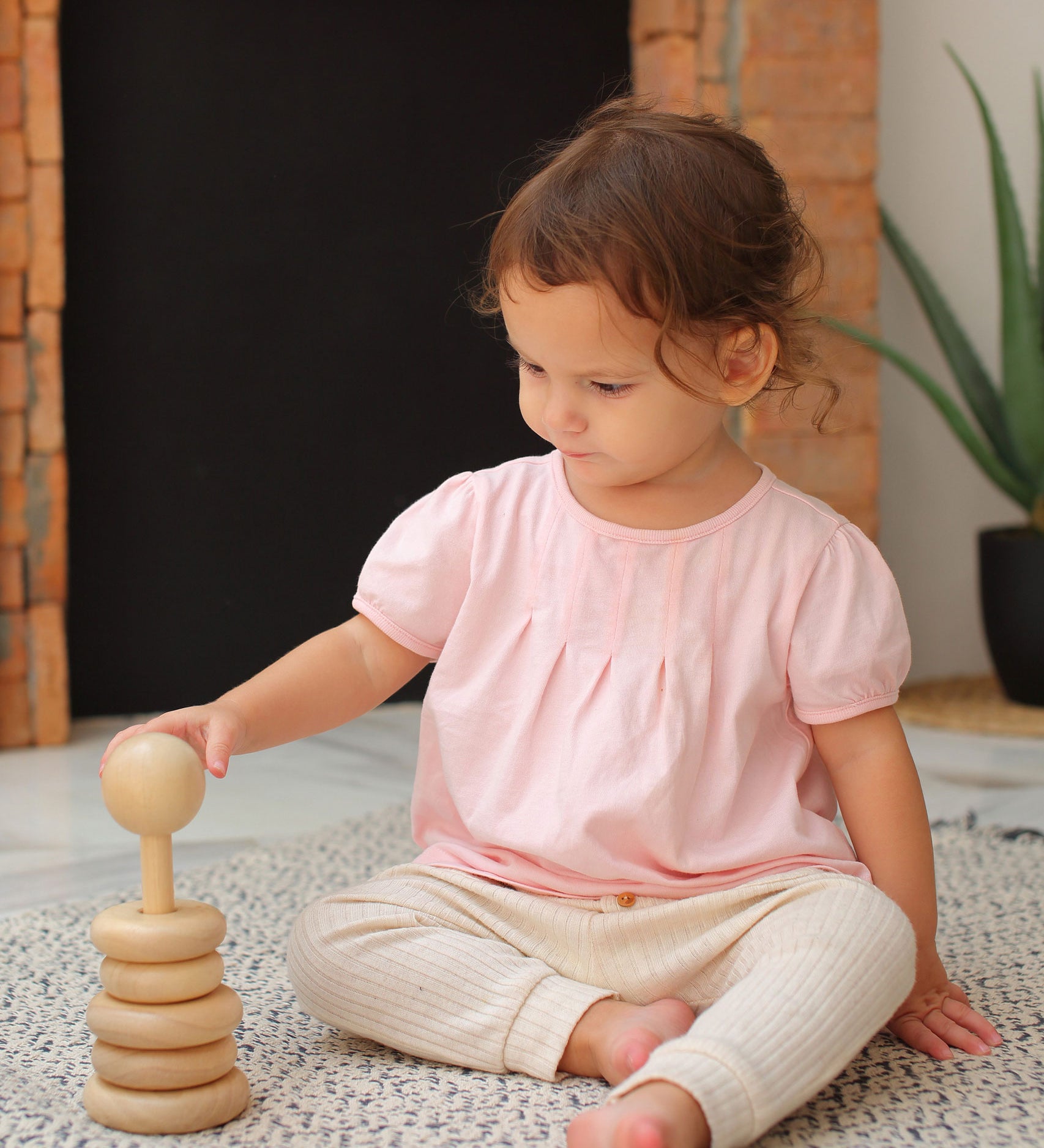 A child sitting on a blue and white rug playing with the Plan Toys Natural Stacking Ring.