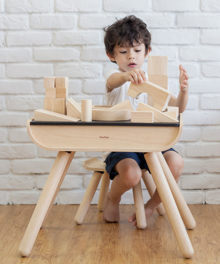 A child sat at a PlanToys desk  playing with the Plan Toys natural wooden 50 Unit Building Block. set.