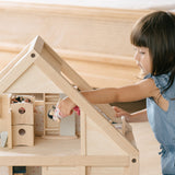 Close up of young girl leaning over to put a small doll toy inside the PlanToys handmade wooden dollhouse