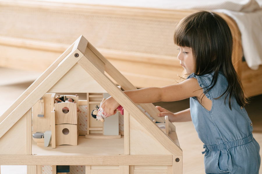 Close up of young girl leaning over to put a small doll toy inside the PlanToys handmade wooden dollhouse