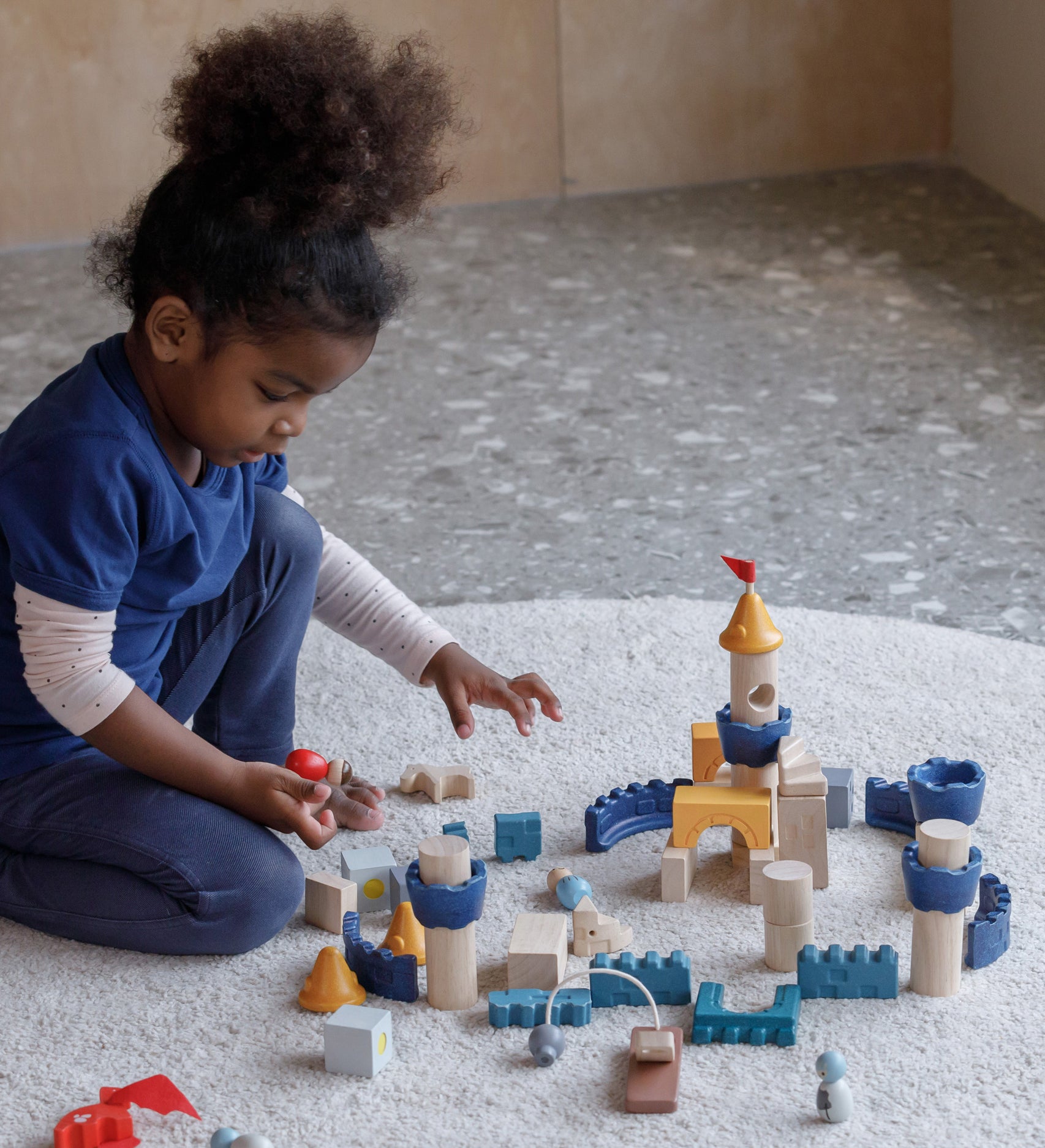 A child playing sitting on a rug playing with the PlanToys Castle Building Blocks set. 