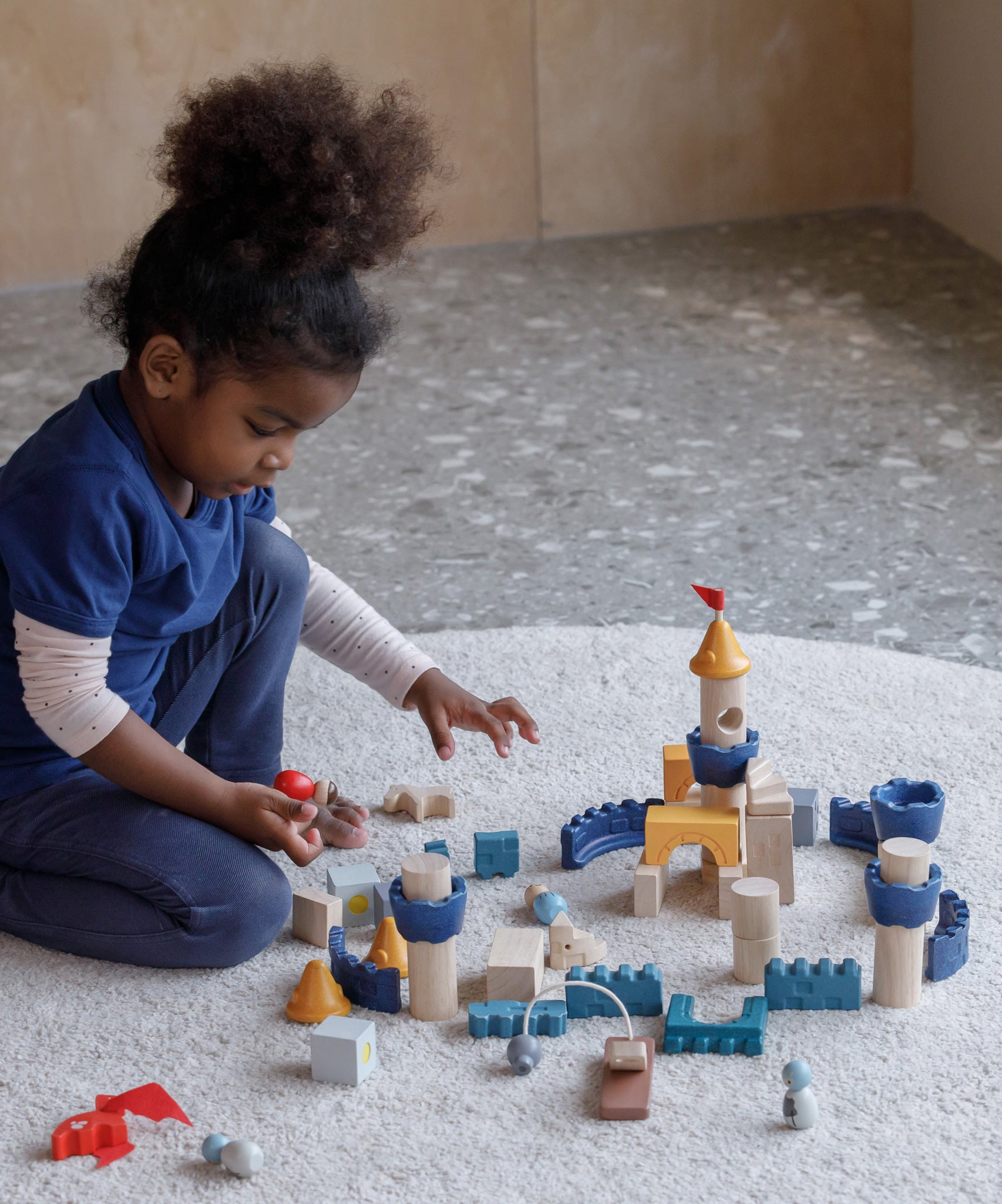 A child playing sitting on a rug playing with the PlanToys Castle Building Blocks set. 