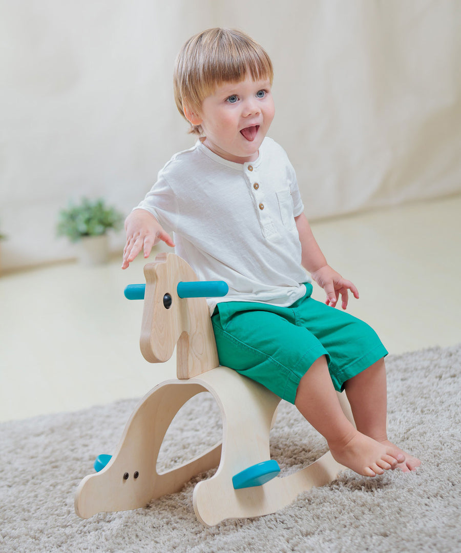 A child sitting on the side of the PlanToys Palomino Rocking Horse. 