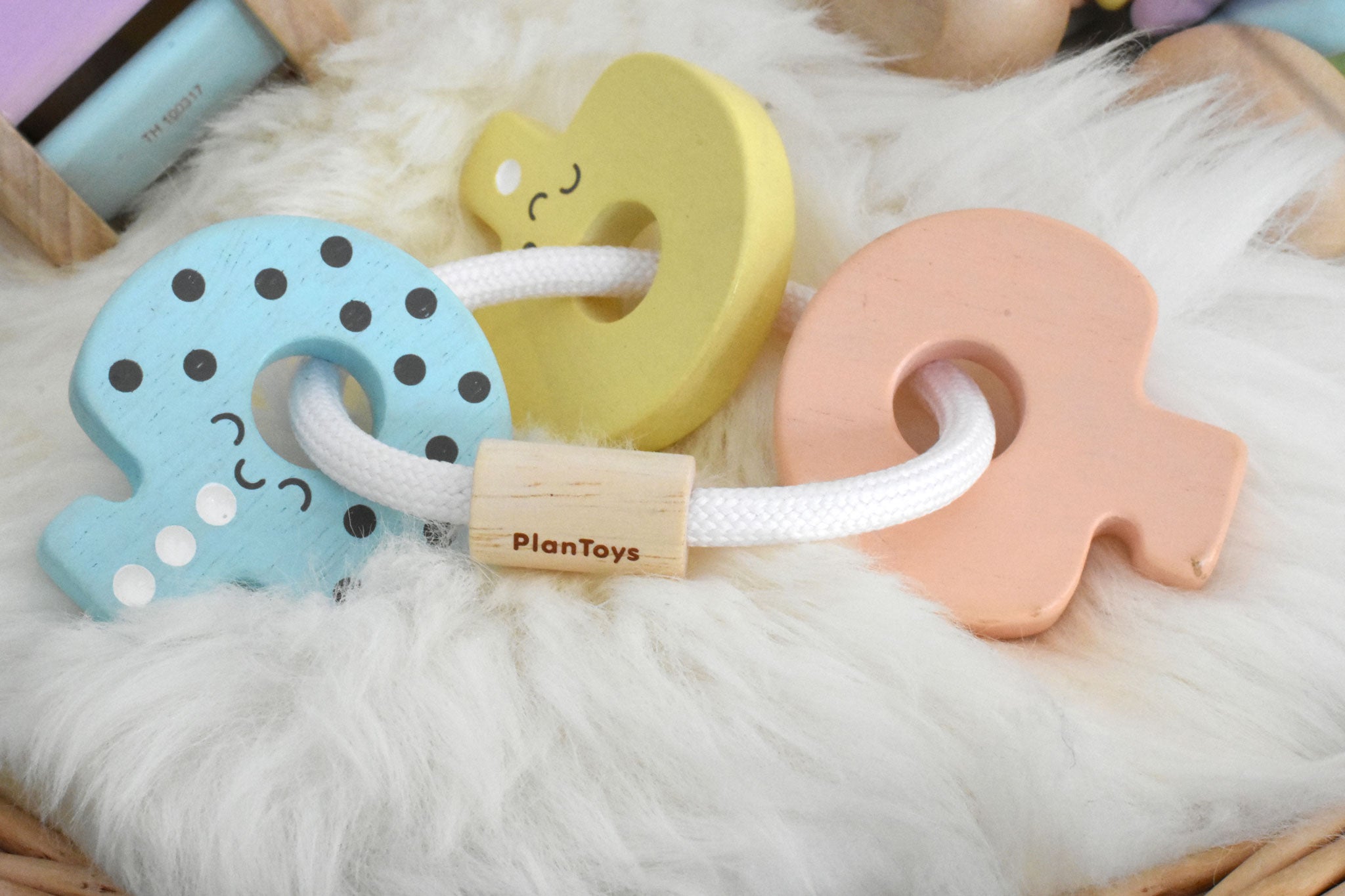 A PlanToys Pastel Baby Key Rattle toy placed on a sheepskin rug. 