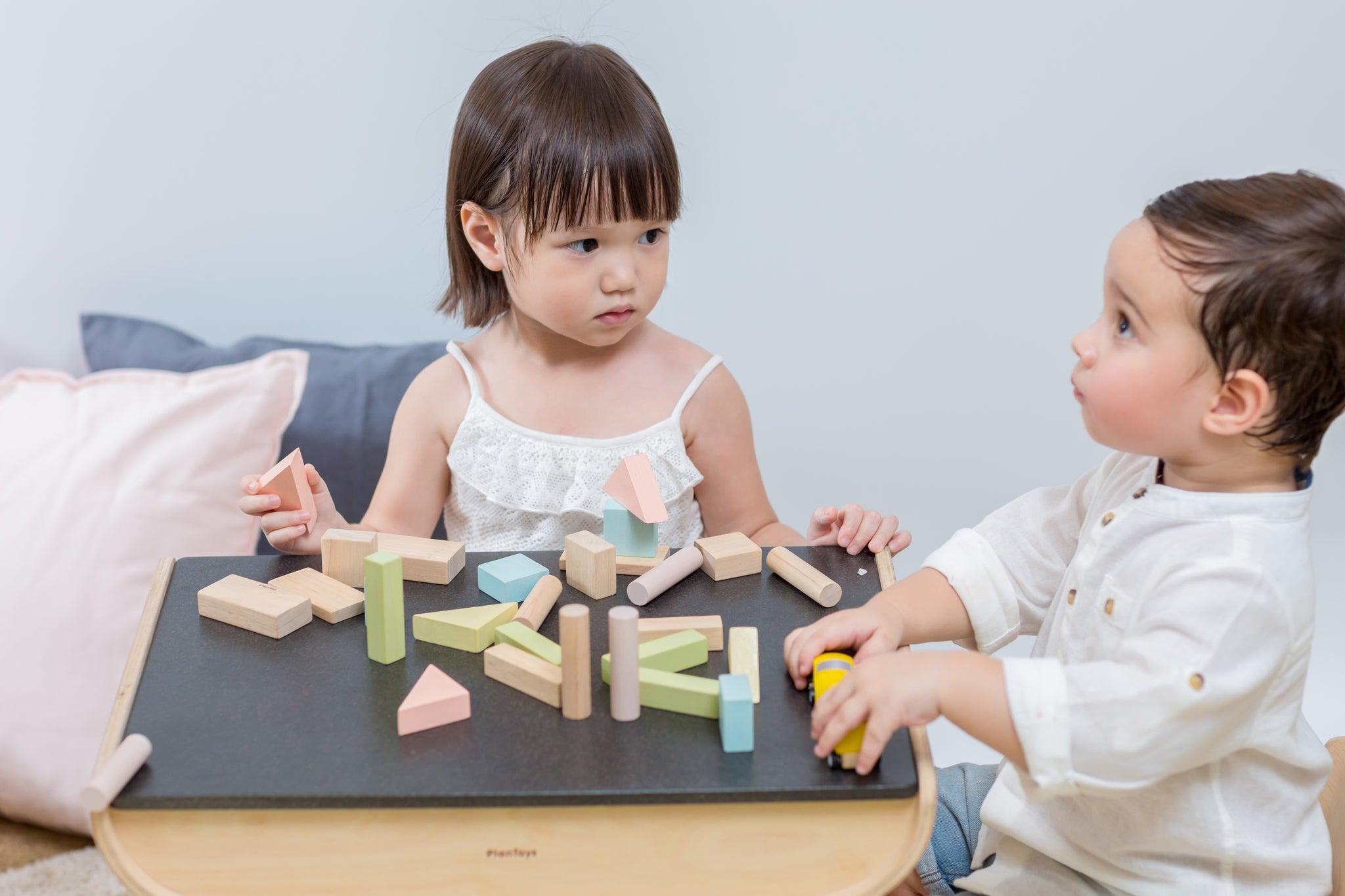 Two children sitting at the PlanToys desk playing with the PlanToys Pastel Blocks set. 